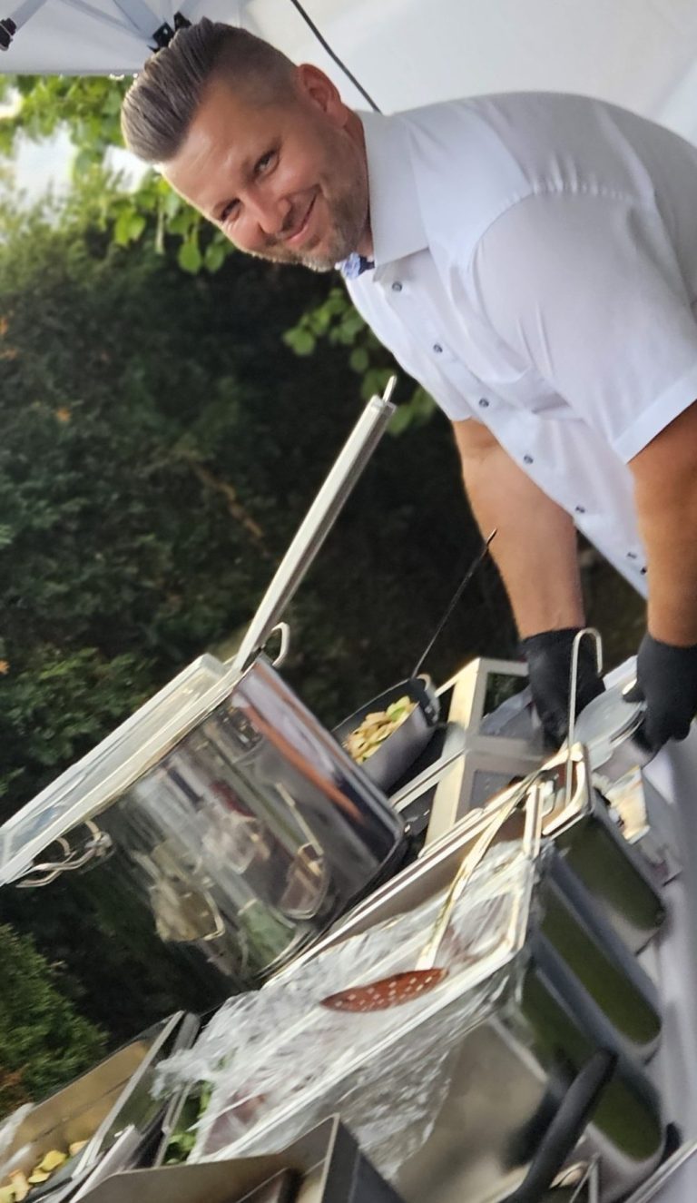 Ein Koch mit Handschuhen bereitet Speisen im Freien vor.